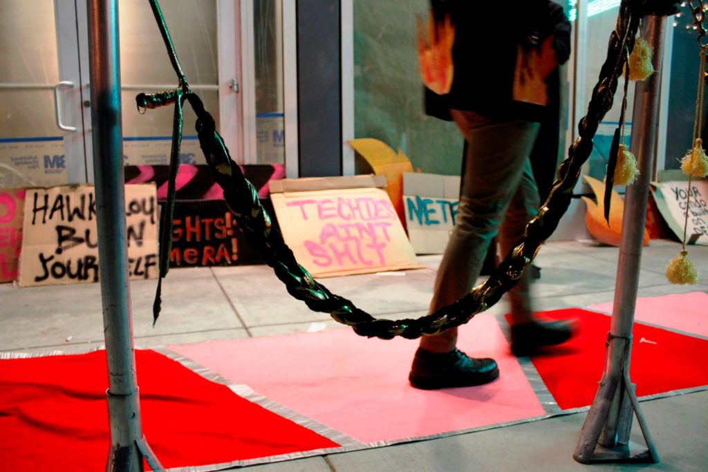 close up a person's feet passing on the red carpet by the stanchion and a row of various protest signs decorating the vacant ground floor retail of the vida luxury condo complex