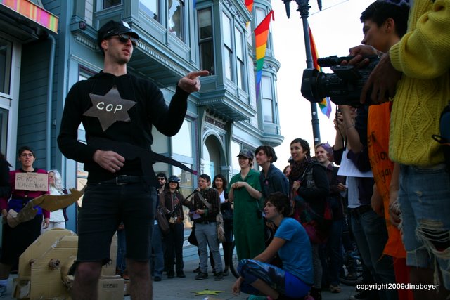 The person portraying a cop is pointing the crowd.