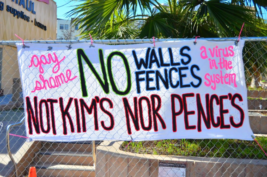 Banner tied to the hurricane fence at McCoppin Hub in the Mission reads "No Walls No Fences, Not Kim's Nor Pence's. Gay Shame: A virus in the system."