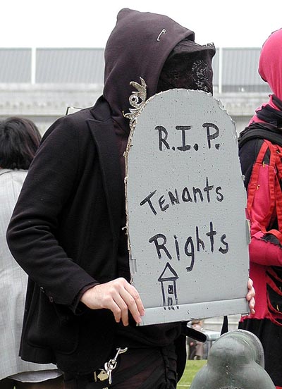 person carrying cardboard tombstone reading "r.i.p. tenants rights"