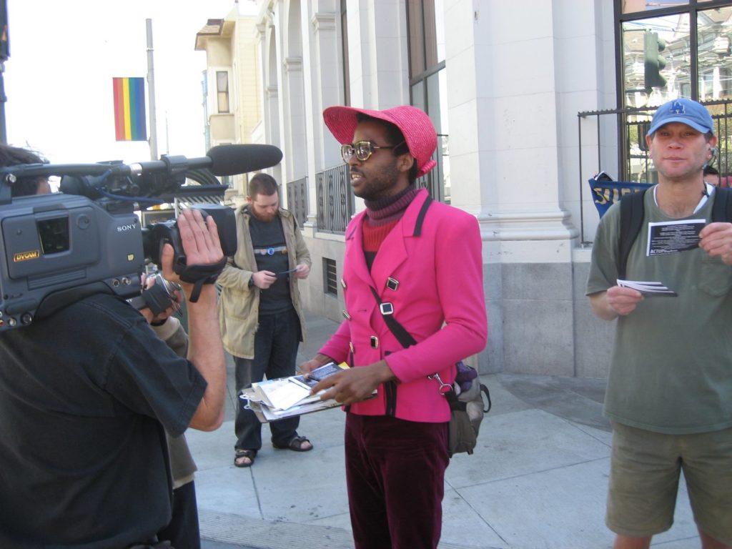 a person is being interviewed by television media at the meet up place for the caravan on castro at 18th