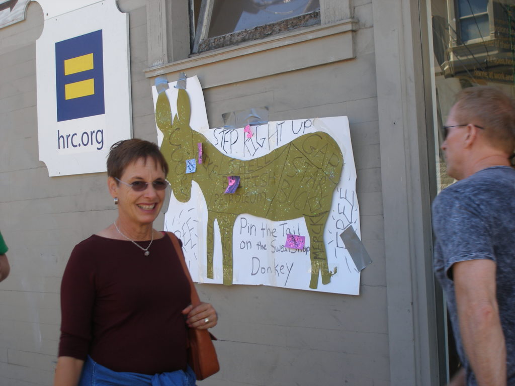 a person apparently delighted to be standing next to pin the tail on the sweatshop donkey on the exterior of the hrc.org shop on castro and 19th