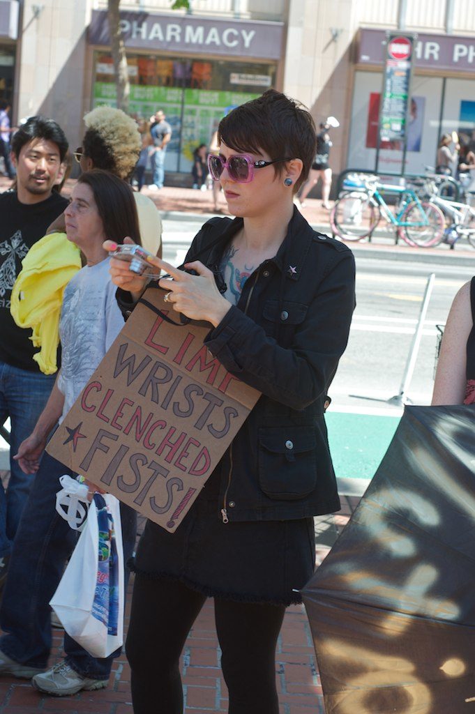 person holding a sign that says "limp wrists clenched fists"