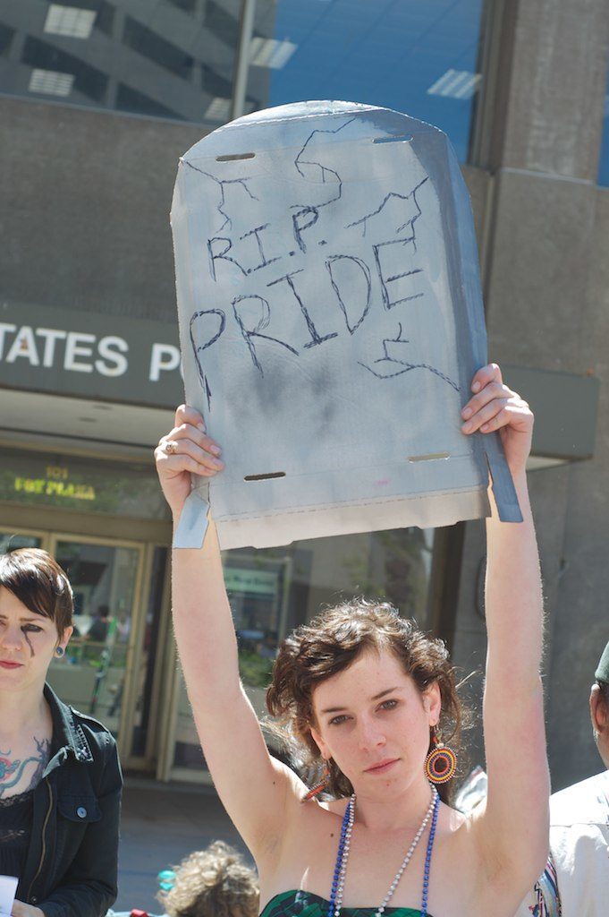 person holding up a cardboard tombstone that reads "r.i.p. pride"