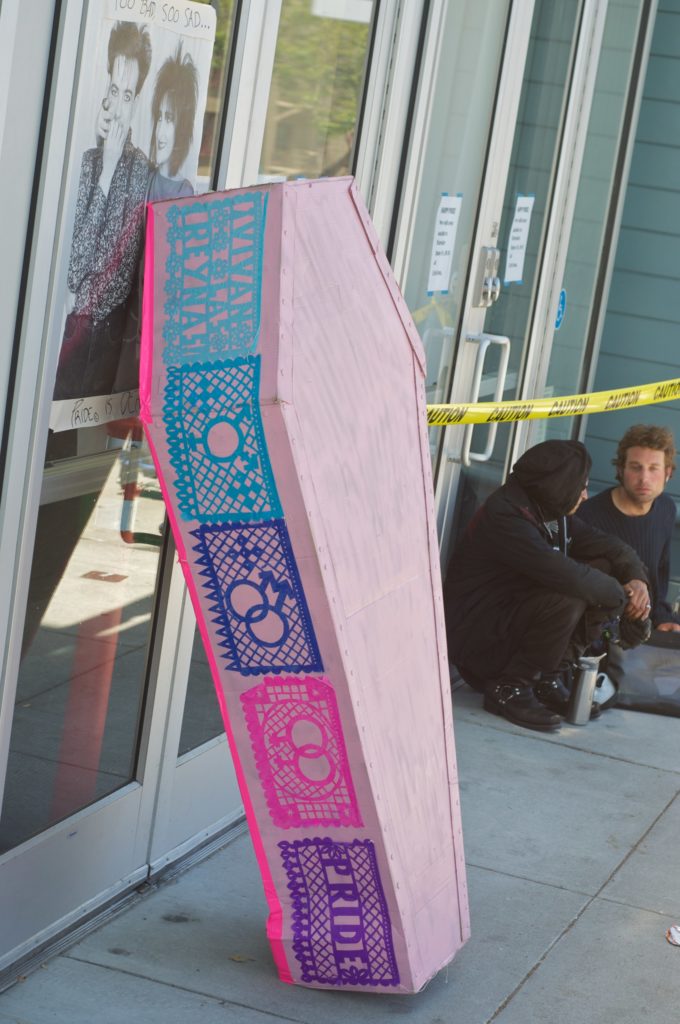 pink cardboard coasted plastered with queer multicolor papel picado leaning against the front entrance of the lgbt center