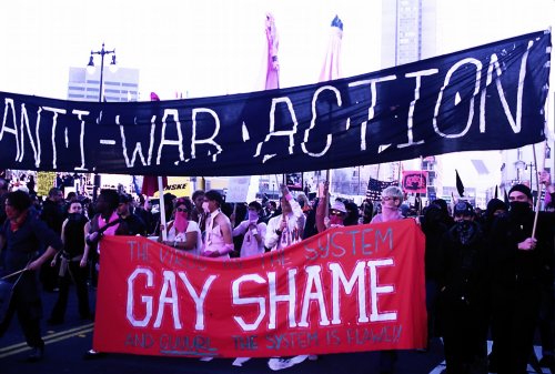 a crowd of people forming a black bloc with a large black banner reading "anti-war action" and underneath a red "gay shame" banner