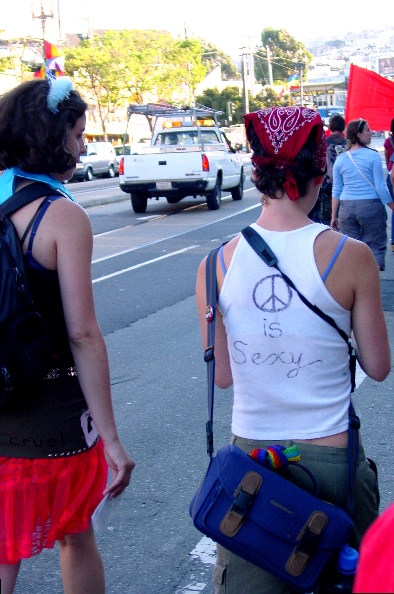 two people walking the walk of shame down market street toward the castro, one wears a t-shirt that says "(peace sign) is sexy"