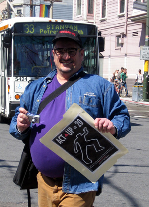 a person holding an act up 20 poster and a mini digital camera as the 33 stanyan bus pulls into the stop at 18th and castro
