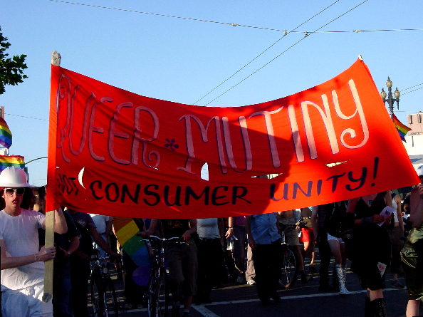 the procession led by the red "queer mutiny not consumer unity" banner continues as the sun goes down