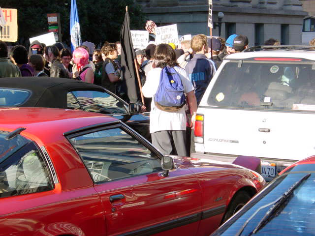 view from within a gridlock of cars stuck in traffic as people with signs and banners move in the background