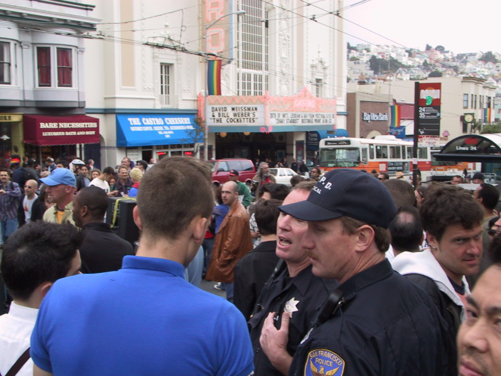 a crowd fills castro and market after the awards ceremony and two police officers complain to awards ceremony attendees