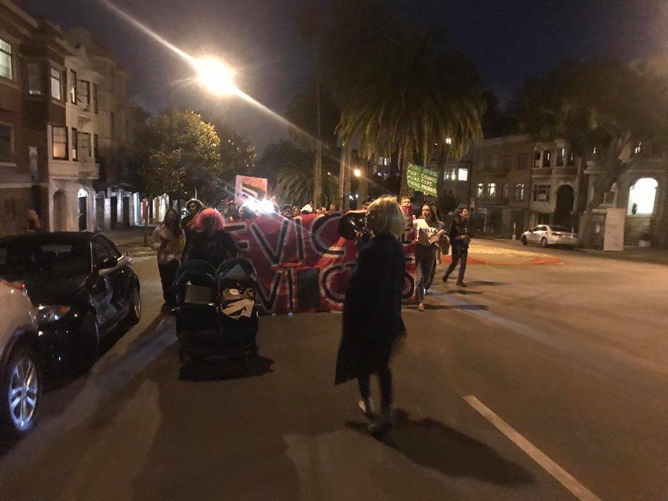 the procession makes its way up dolores with a "evict the evictors" banner out in front