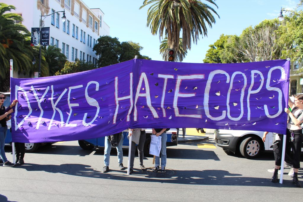 people holding a purple banner reading "dykes hate cops"