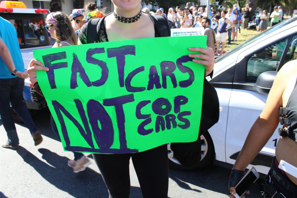 person holding a sign reading "fast cars not cop cars"