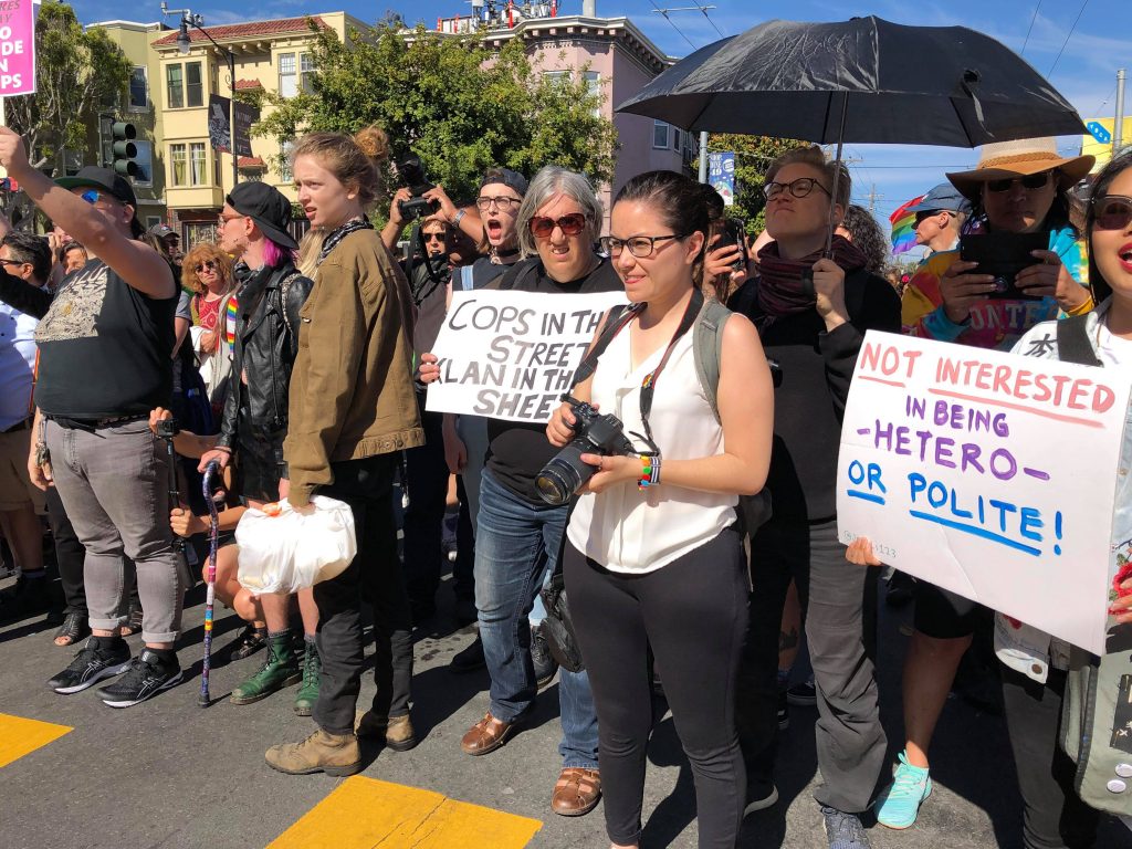 people gathered at the intersection of 18th and dolores holding signs that read "cops in the streets --- klan in the sheets" and "not interested in being -hetero- or polite!"
